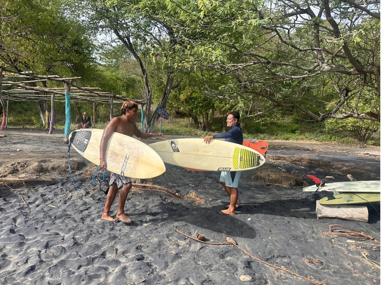 Two surfers carrying boards toward the beach in Gigante, Nicaragua